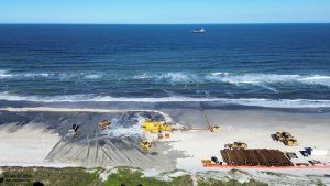 An oblique aerial photograph of the beach fill screening operations (29-March-2024).